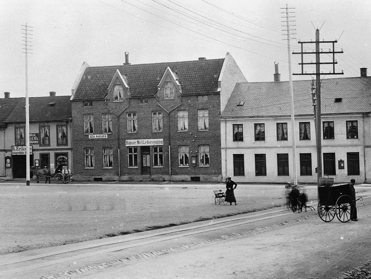 Hans Emil Erichsen, Østre Torg i Hamar med bebyggelsen langs Vangsvegen. Postkontor, Hamar Melkeforsyning, Agra Margarin, R. Eriksens Fotografiske Atelier. J. Skaraasen Agentur. Folk på torget. Hest og kjerre med melkespann. Utsnitt.