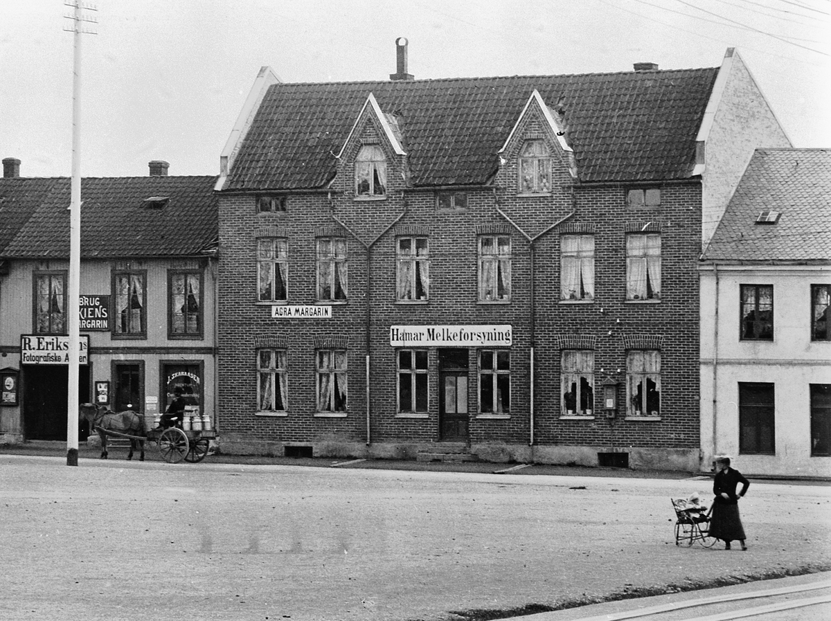 Hans Emil Erichsen, Østre Torg i Hamar med bebyggelsen langs Vangsvegen. Hamar Melkeforsyning, Agra Margarin reklame, R. Eriksens Fotografiske Atelier. J. Skaraasen Agentur. Dame med barnevogn på torget. Hest og kjerre med melkespann. Utsnitt.