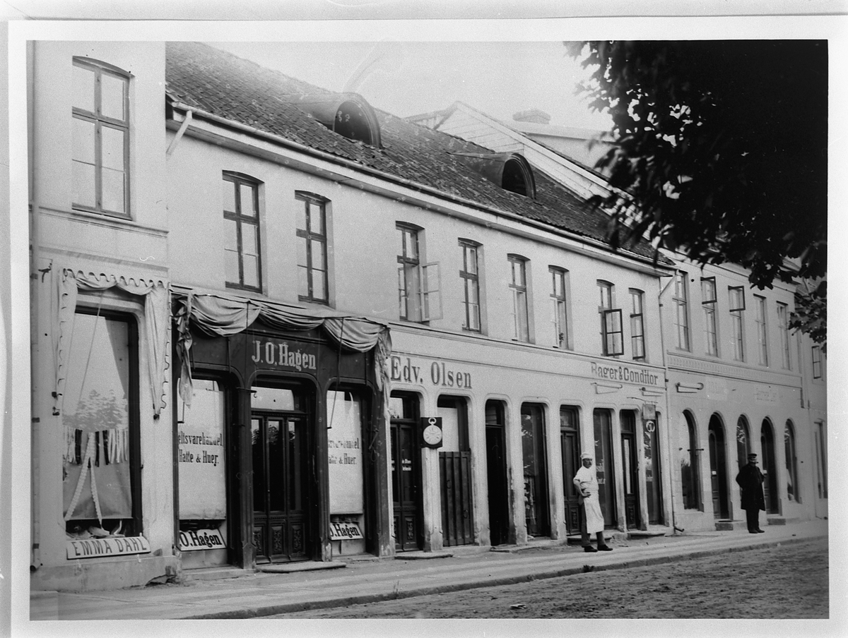 Hans Emil Erichsen, Strandgata 41-43 i Hamar. Forretningene til Emma Dahl, J.O. Hagen, Bager & Conditor Edv. Olsen, J.O. Lier og søstrene Lier. Personene på bildet er bakermester B. Opsahl og tannlege C. Opsahl.