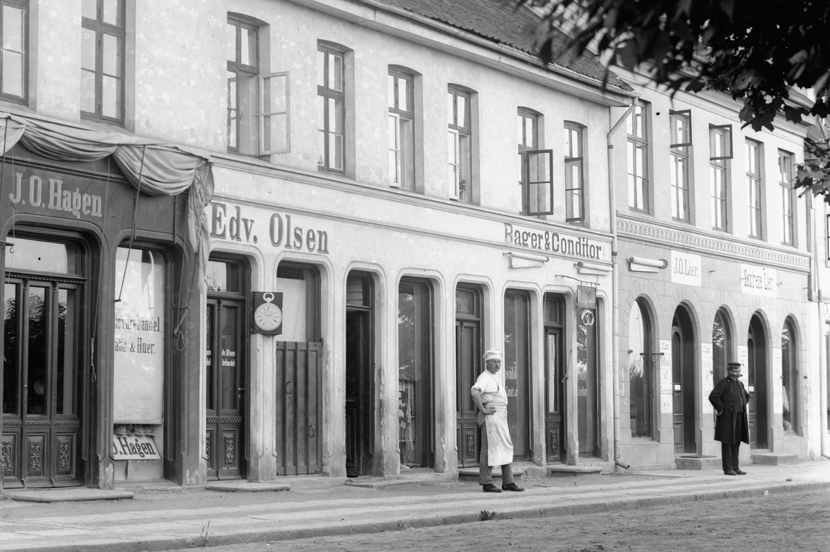 Hans Emil Erichsen, Strandgata 41-43 i Hamar. Forretningene til Emma Dahl, J.O. Hagen, Bager & Conditor Edv. Olsen, J.O. Lier og søstrene Lier. Personene på bildet er bakermester B. Opsahl og tannlege C. Opsahl.
