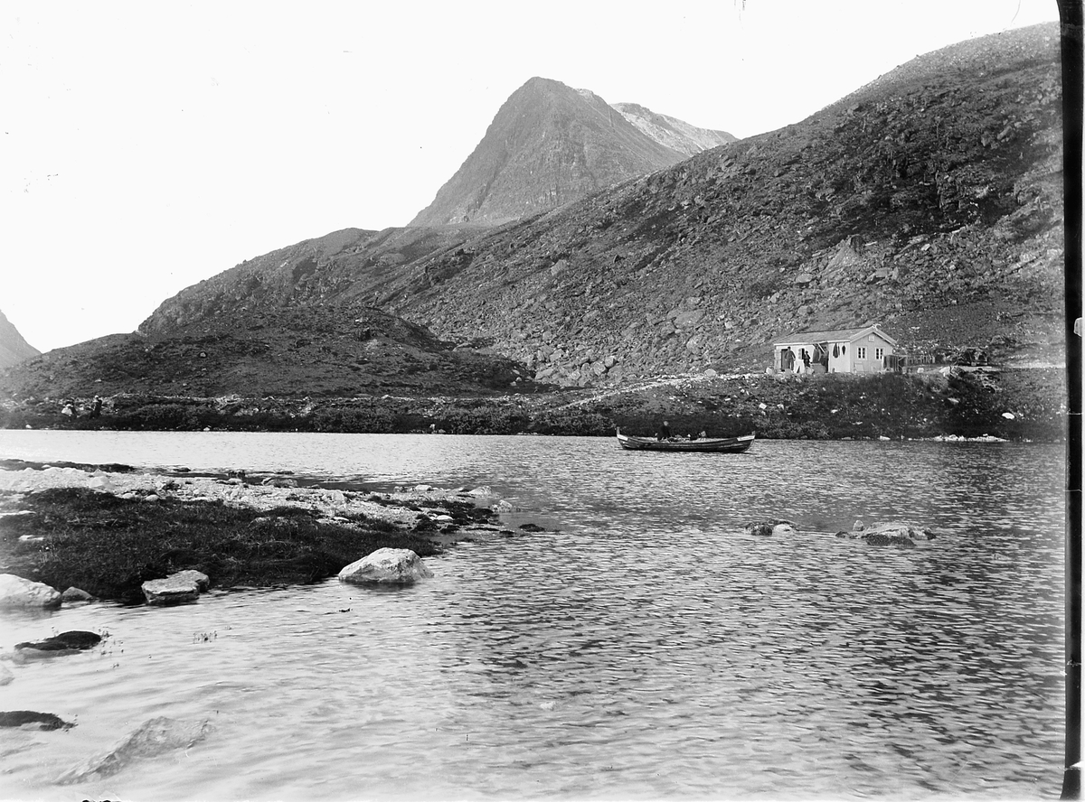 Simen Baardseth, RONDANE, Rondvatnet. En person i robåt. Hytta i bakgrunnen er Rondvassbu slik den så ut først i 1920-årene.