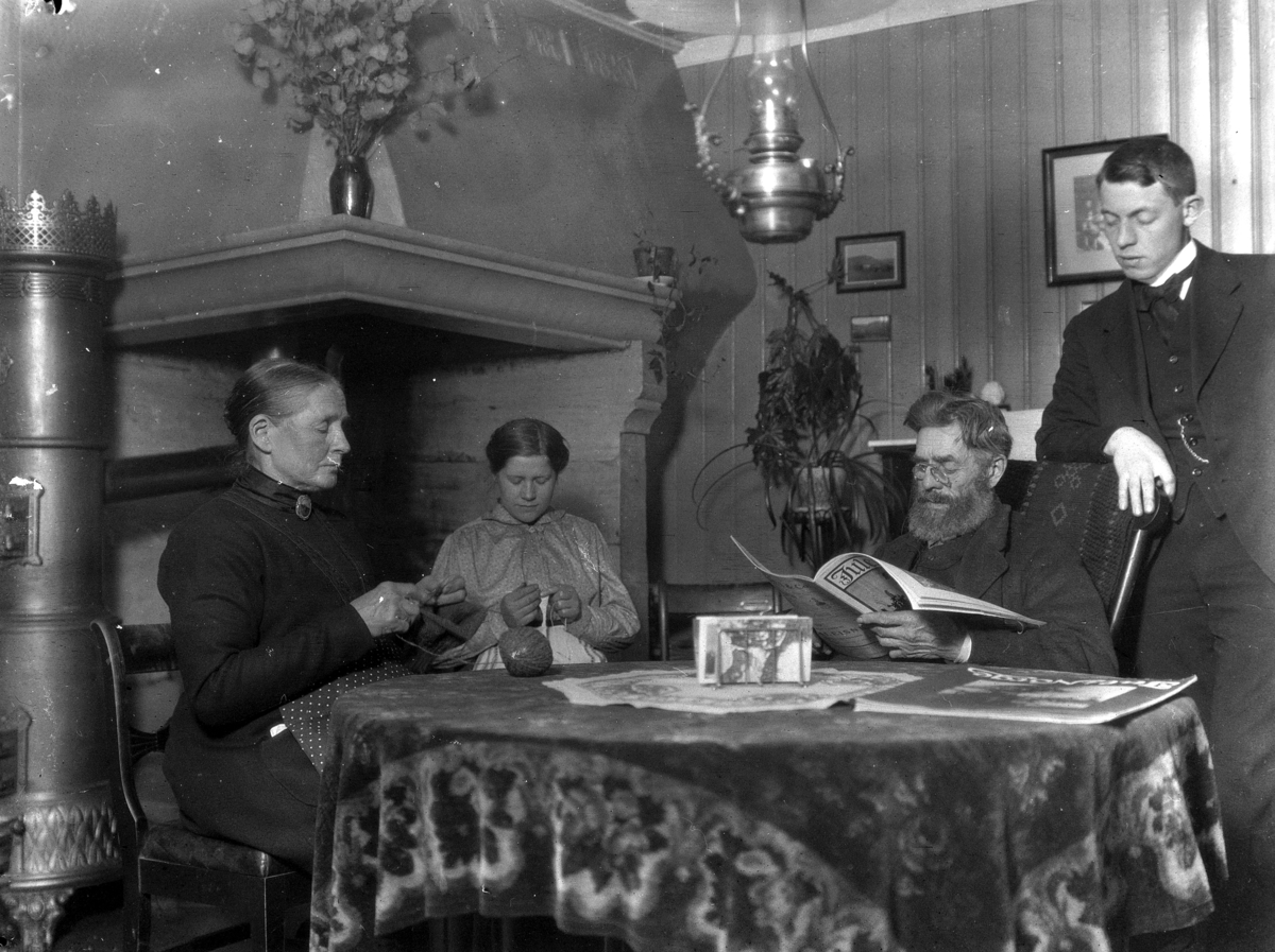 Kristian Heramb, Gr. 4. Familien samlet ved stuebordet. Kvinnene strikker, Andreas Heramb leser. "Far læser høit".