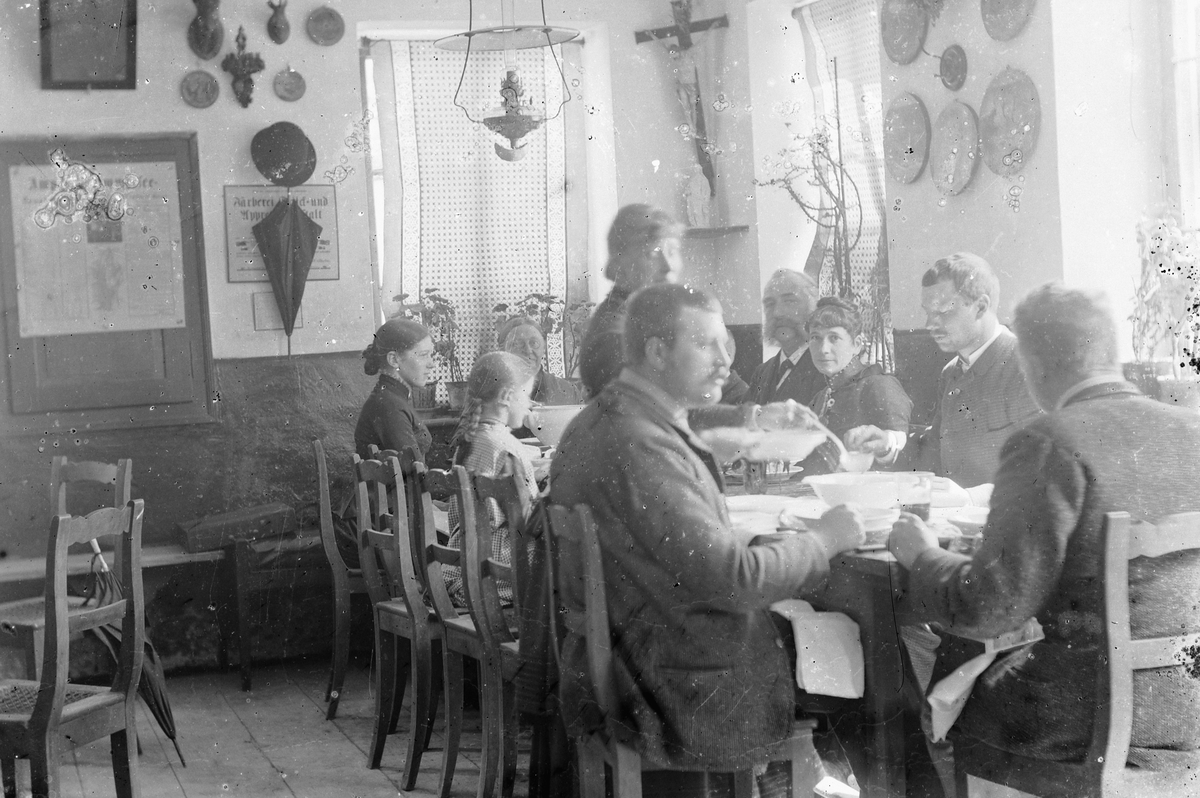 Hans Emil Erichsen, Voksne og barn rundt spisebord. Mye pynt på veggene. Kristusfigur. Tyskland.