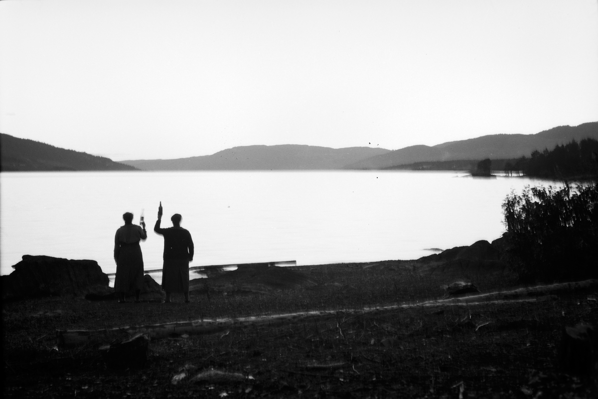 Håkon Prestkværn, To ukjente menn med hver sin brennvinsflaske ved vannkanten. Mjøsa.