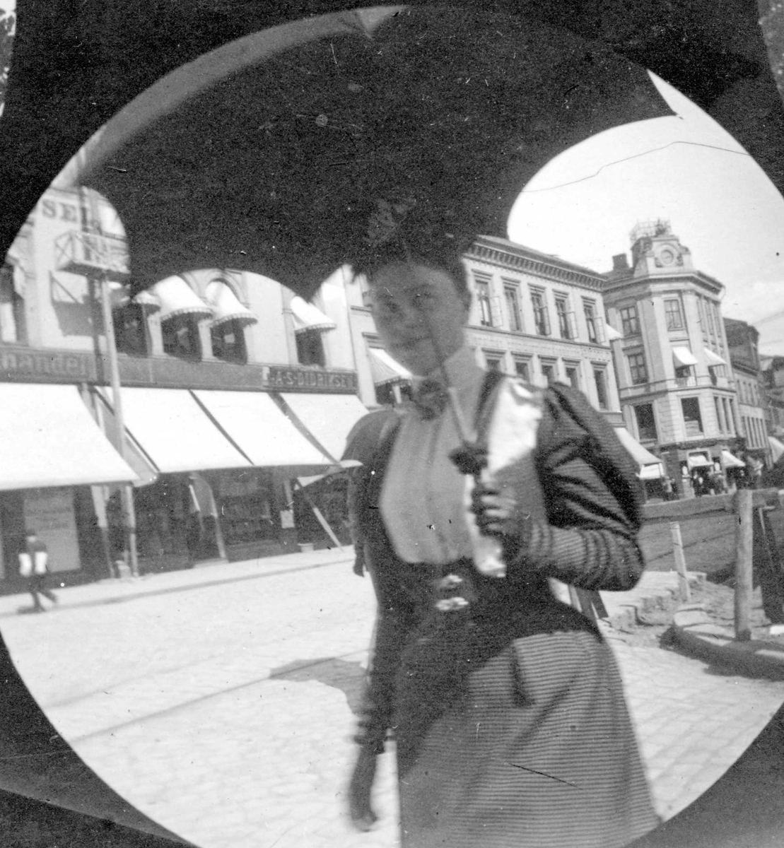 Fredrik Carl Mülertz Størmer, Frk. Marie Reimers spaserer langs bygate. foretningsbygg med markiser og brosteinsarbeid.