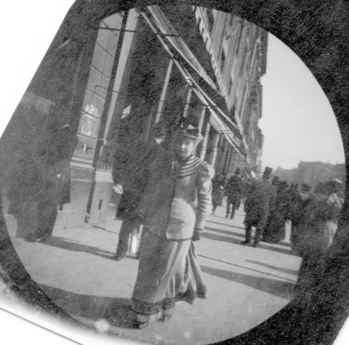 Fredrik Carl Mülertz Størmer, Mennesker spaserer langs butikker på Karl Johans gate, Oslo. Stortinget skimtes. Frk. Johanne Nissen, senere gift Scheel, midt i bildet.