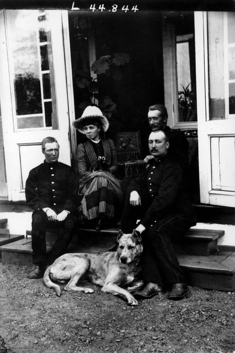 Fredrik Emil Faye, Gruppeportrett, person gruppe med hund i inngangsparti. Fra venstre Jakhen(?) Heftye, fru Sigrid Faye, Frølich, T. Heftye, ca.1880. Fra portrettserie av personer som bodde på eller besøkte Dal gård, Ullensaker, fotografert av gårdens eier, kammerherre Fredrik Emil Faye (1844-1903) i årene 1875-1900.