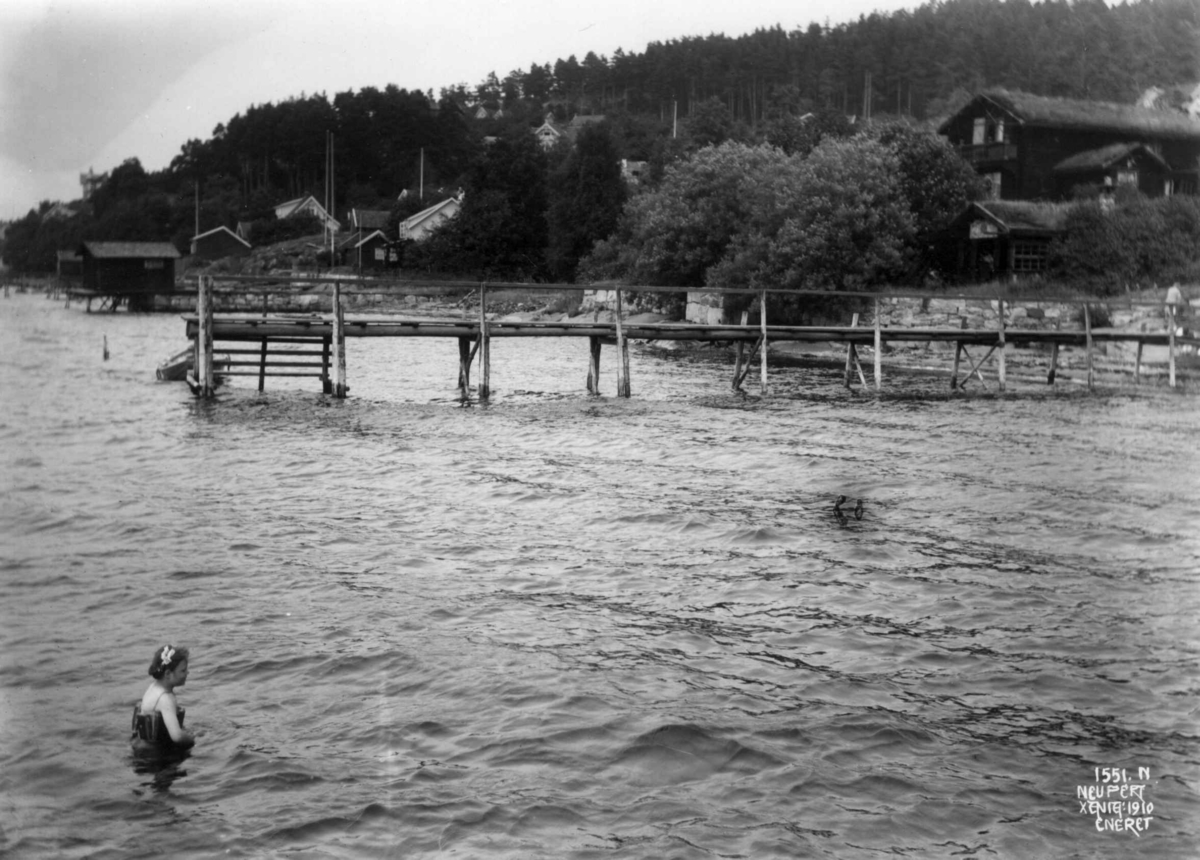 Hermann Christian Neupert, Thorkelbyen, Drøbak, Frogn, Akershus 1910. Hus og brygger langs stranda. Jente bader.