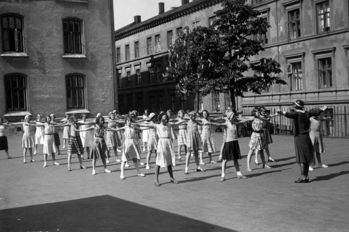 Hermann Christian Neupert, Ruseløkka skole, Oslo. 1932. Skolegymnastikk i skolegården. Lærerinne instruerer småjenter.