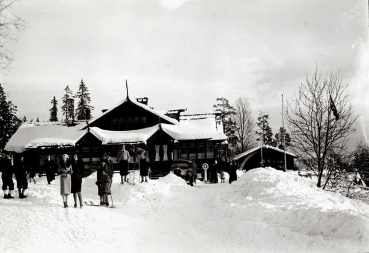 Hermann Christian Neupert, Frognerseteren Restaurant, Nordmarka, Oslo. Vintermotiv. Mennesker på ski foran resturanten.