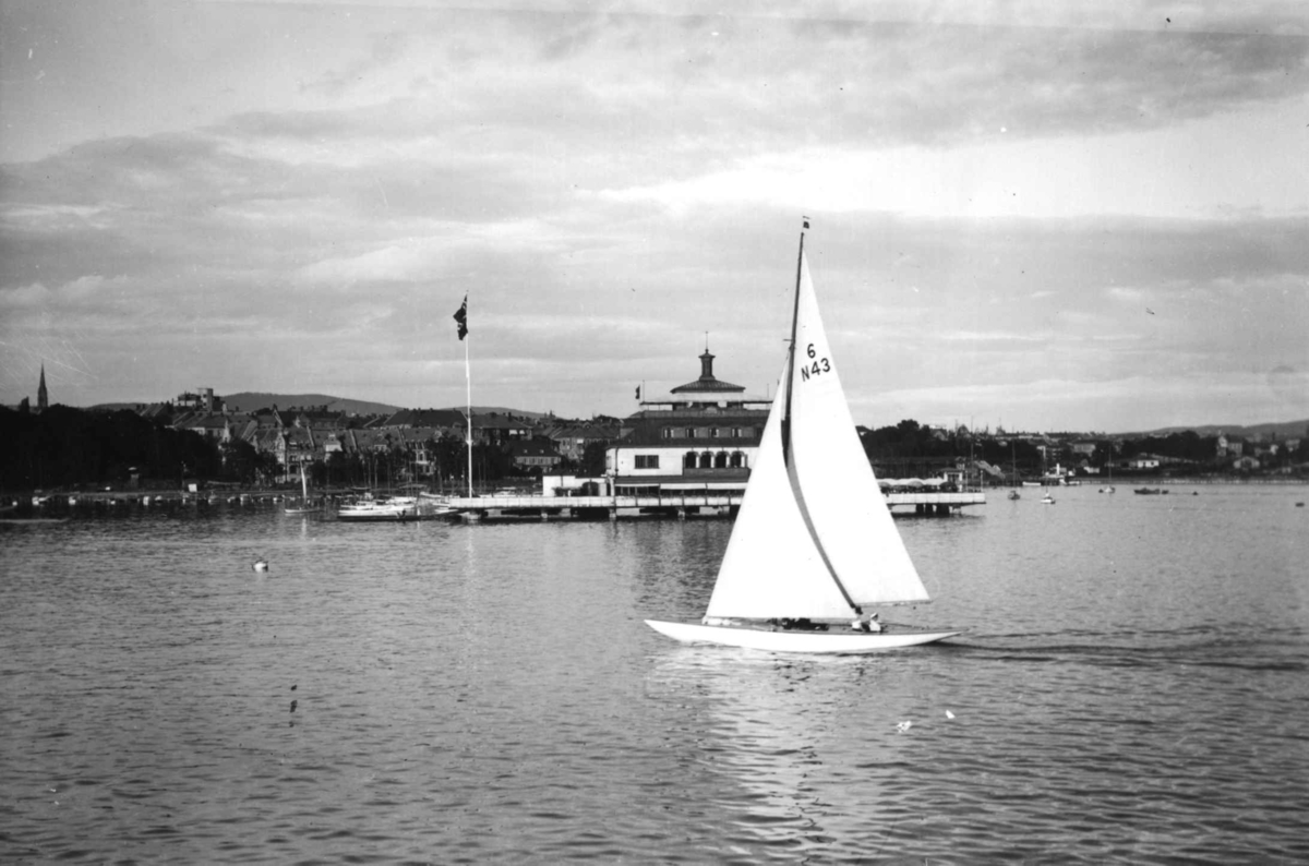 Hermann Christian Neupert, Frognerkilen, Oslo. Seilbåt foran restaurant Kongen. Byen i bakgrunnen. Flagg.