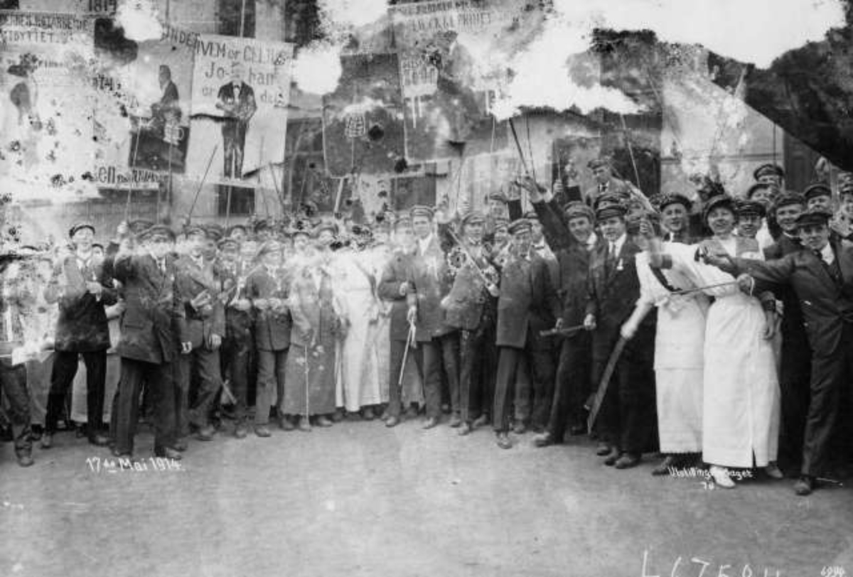 Hermann Christian Neupert, Oslo. Russ 17. mai 1914. Festkledde i lange kjoler og dress. Russeplakater ses i bakgrunnen.
