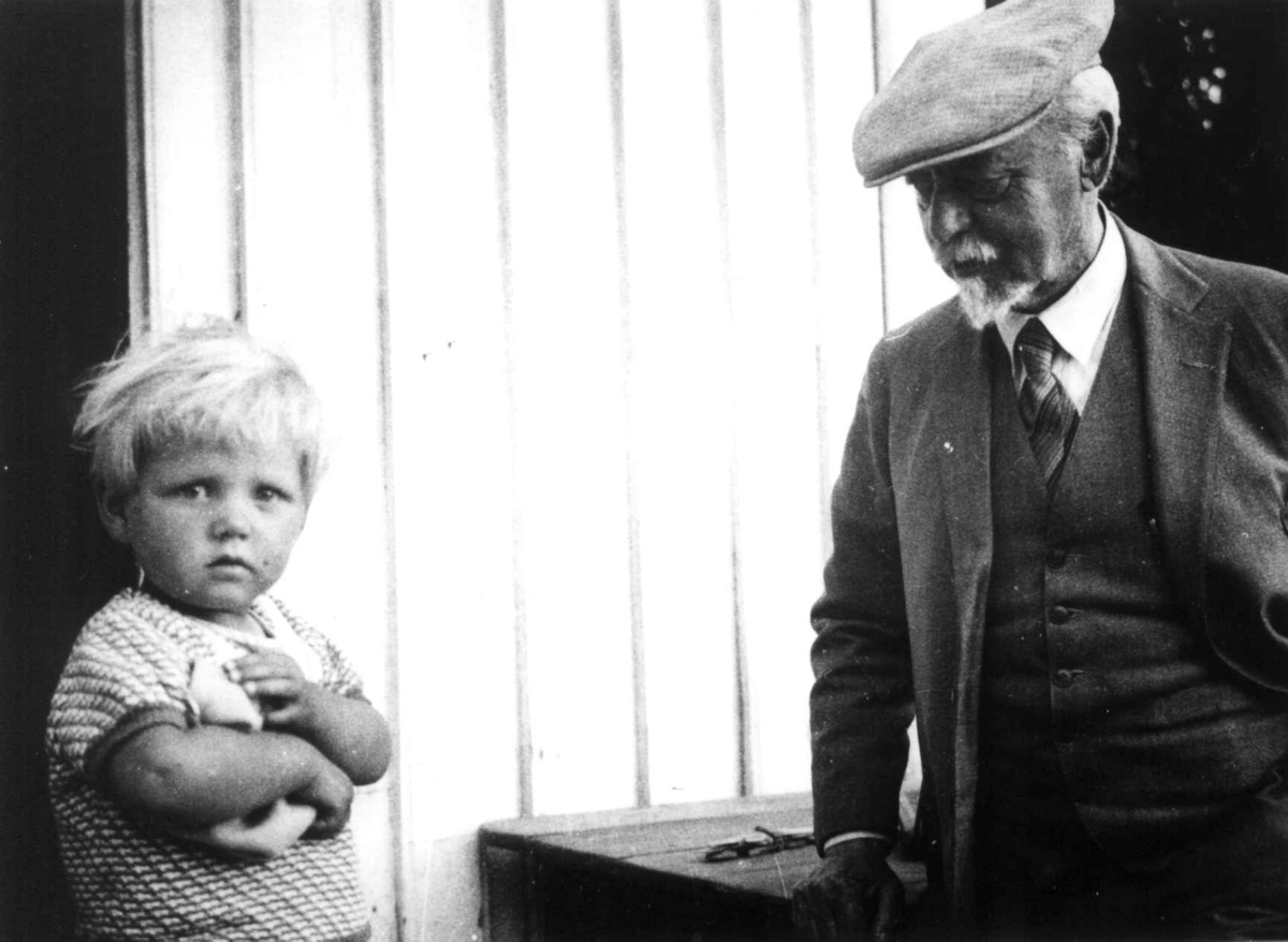 Anna Grostøl, Kunstmaler Müller står henvendt til en liten gutt utenfor et hus. Tveit, Kristiansand 1937.