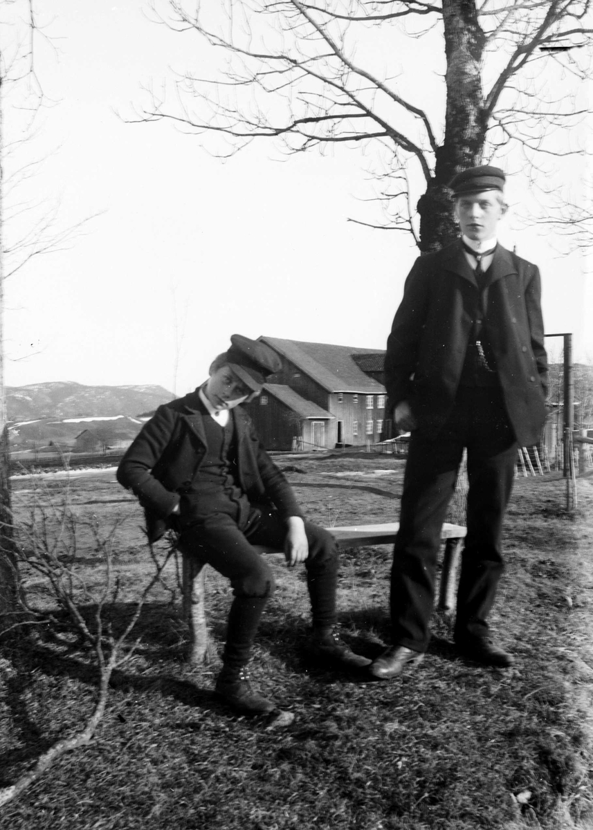 Juliane Fredrikke Langberg, Portrett av 2 gutter med skyggelue, den ene sittende på en benk, foran uthusene til Hurum prestegård. Christian L. Holm t.v. er fotografens nevø, sønn av sognepresten. Gutten t.h. er Olaf Bull, senere forfatter. Fra malerinne Juliane Fredrikke Langbergs (1856-1930) samling, tatt ca.1895-1910 med mo…