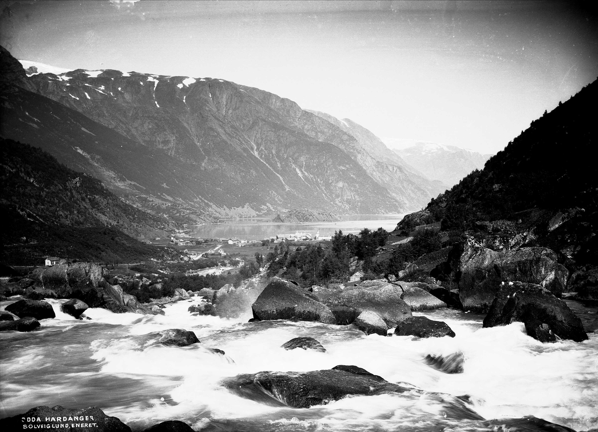 Solveig Lund, Landskapsfotografi fra Odda i Hardanger. I bakgrunnen sees Sørfjorden og i forgrunnen antakelig Opoelva. I midten sees Odda med kirken og Hardanger hotell.