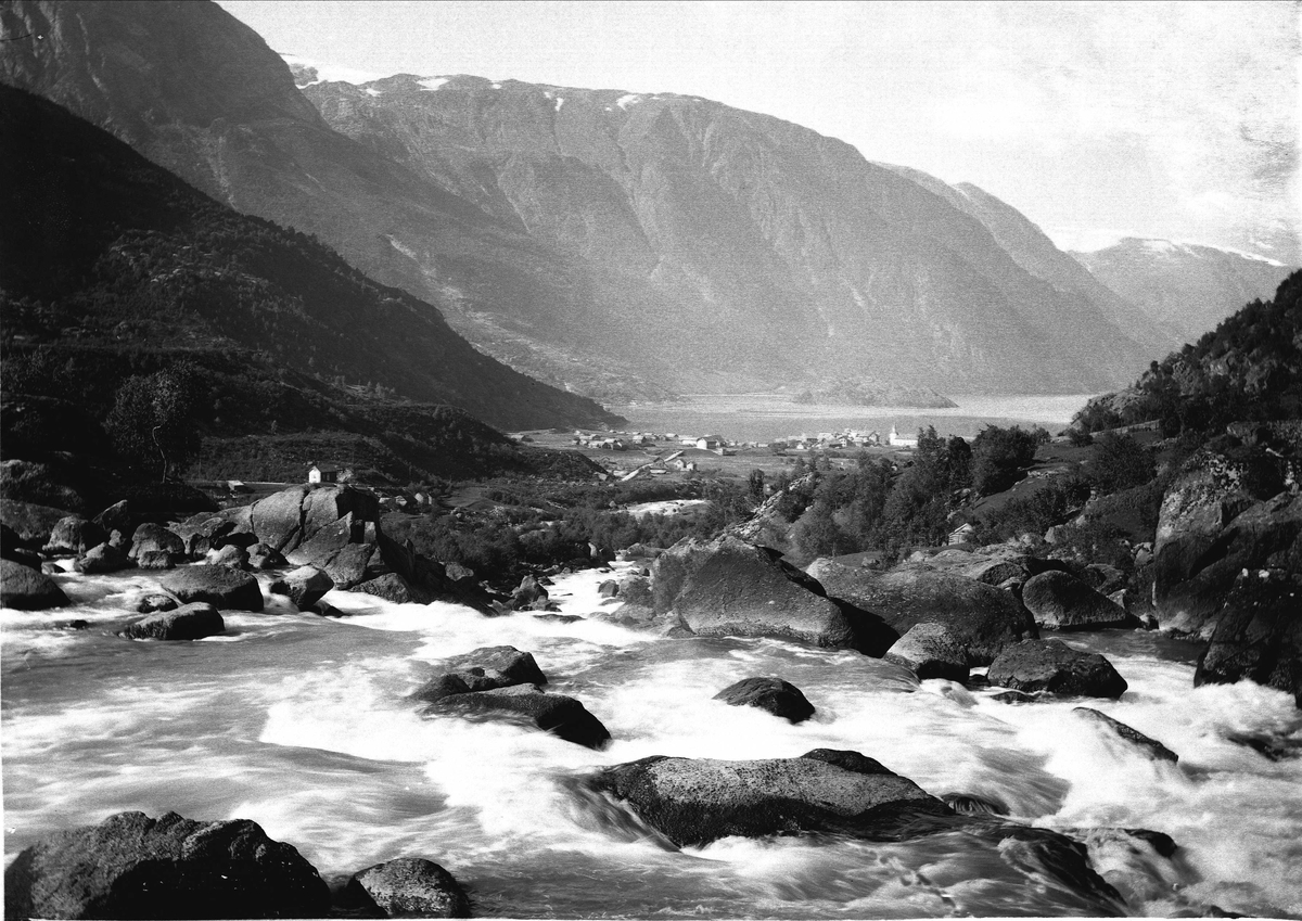 Solveig Lund, Landskapsfotografi fra Odda i Hardanger. I bakgrunnen sees Sørfjorden og i forgrunnen antakelig Opoelva. I midten sees Odda med kirken og Hardanger hotell.