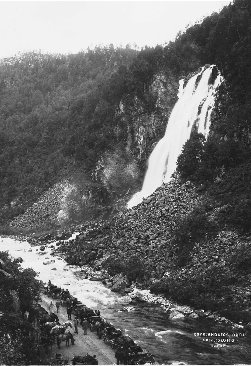 Solveig Lund, Veiparti nær Espelandsfossen ved Odda i Hardanger. Her står flere mennesker på veien og ser opp mot fossen. Hester og kjerrer står "parkert".