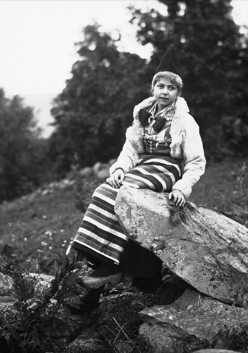 Solveig Lund, Pike i drakt som sitter på en stein - skog i bakgrunnen.