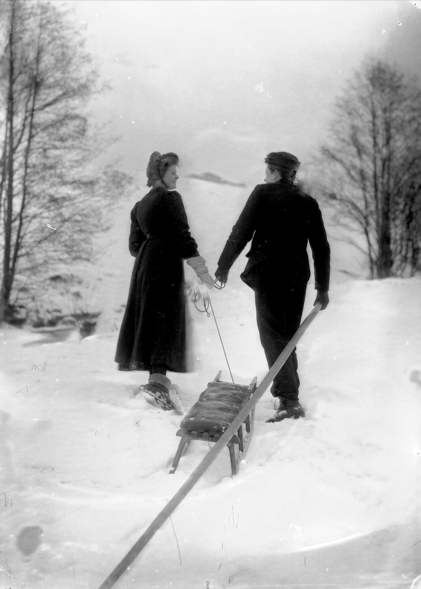 Solveig Lund, Mann og kvinne på tur i snødekt landskap. Fotografert bakfra. De drar en kjelke etter seg.