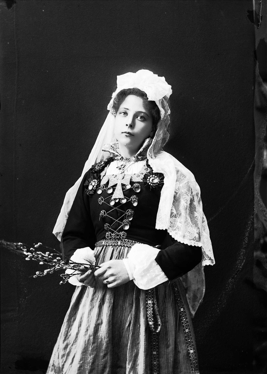Solveig Lund, 3/4 del studioportrett av kvinne i drakt med slør. I hendene holder hun en neve med gåsunger. Hun ser ut mot betrakteren. Nøytral bakgrunn.