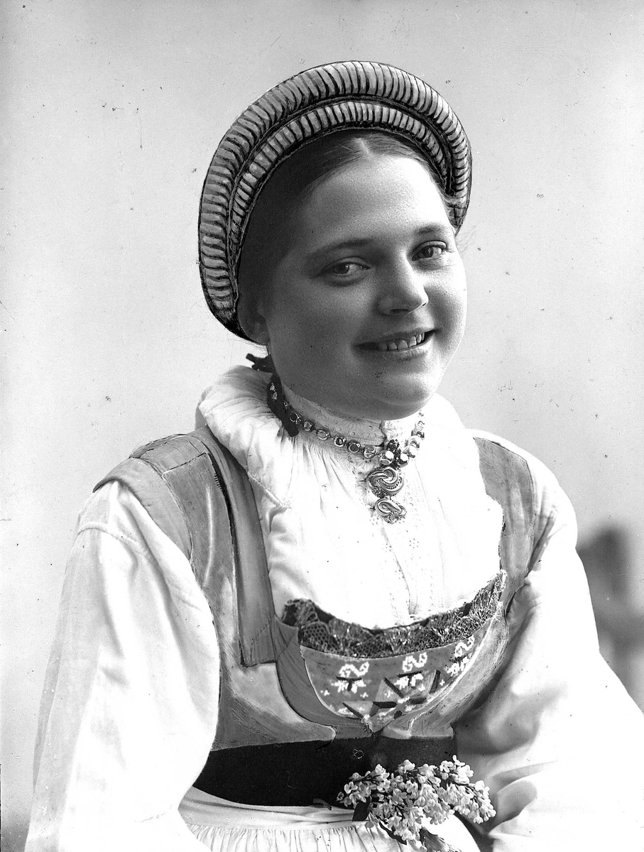 Solveig Lund, Brystportrett av kvinne i drakt og skaut/hatt. Hun sitter og jolder en liljekonval i hendene. Bakgrunnen er nøytral.