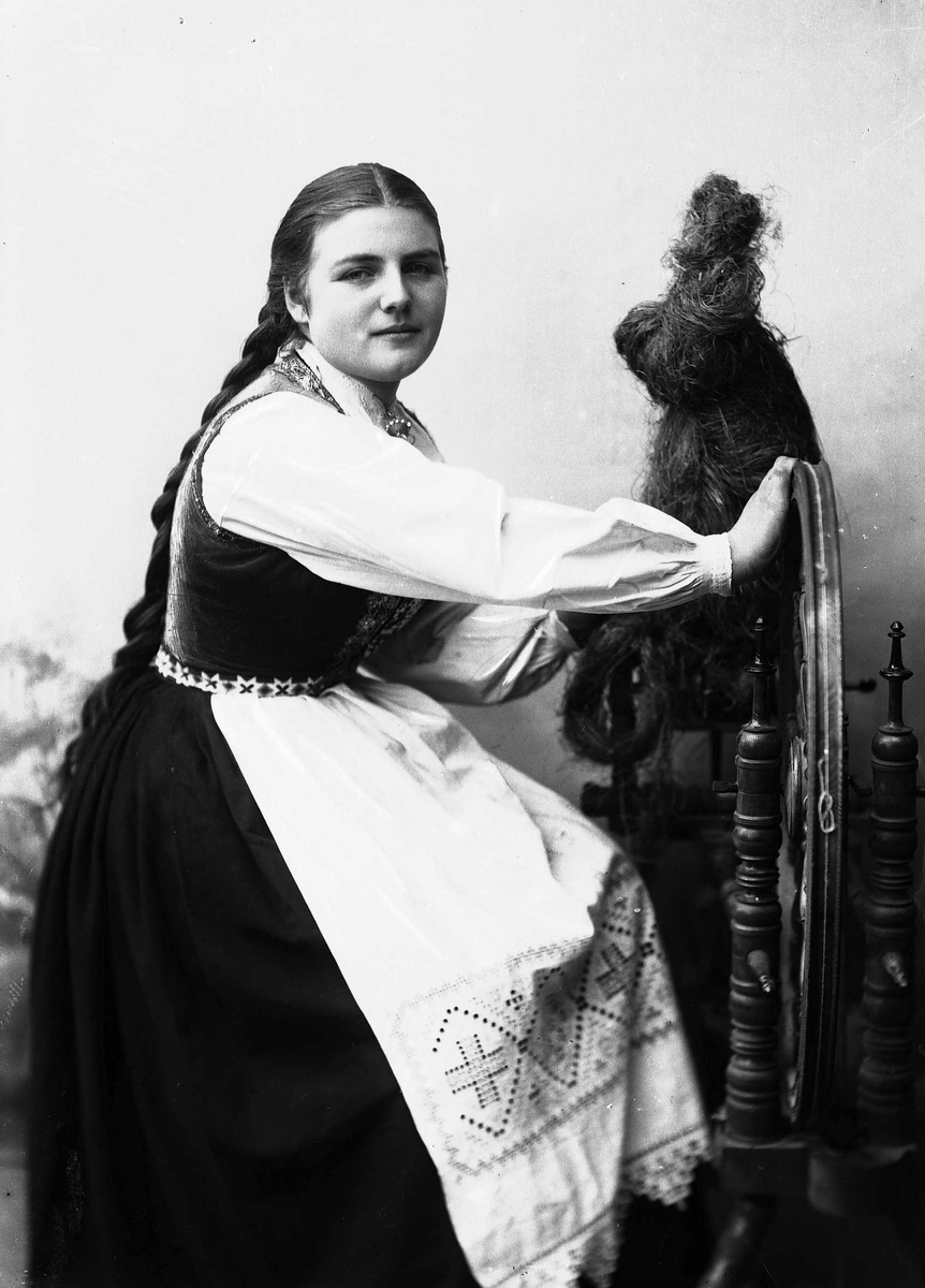 Solveig Lund, Studioportrett av kvinne i drakt og flettet hår, som sitter ved en rokk. Bakgrunnen er nøytral.