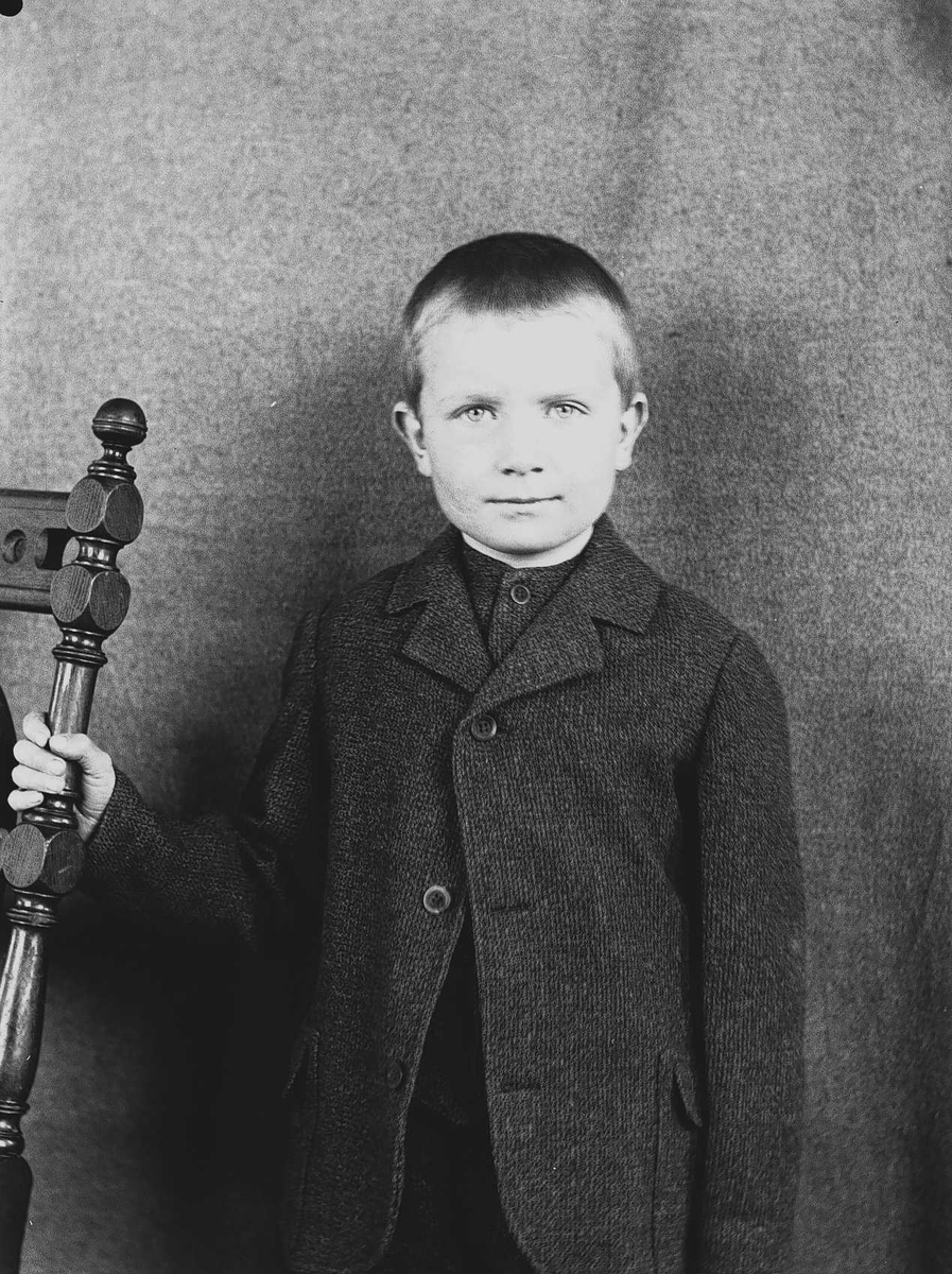 Axel Quinsgaard Wiborg, Portrett av gutt ved stol, Digerud, Frogn, Akershus, 1907. Iflg. fotografen er dette hans sønn Halvor Nicolai Q. Wiborg, men sammenliknet med andre motiver passer dette med Axel, en eldre sønn.