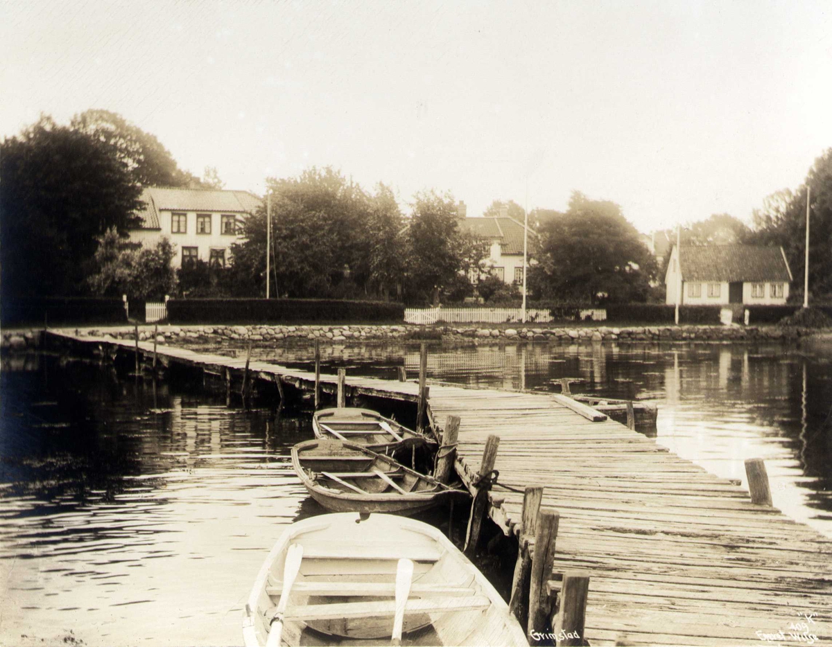 Anders Beer Wilse, Bolighus ved sjøen, Grimstad, Aust-Agder. Brygge med robåter i forgrunnen.