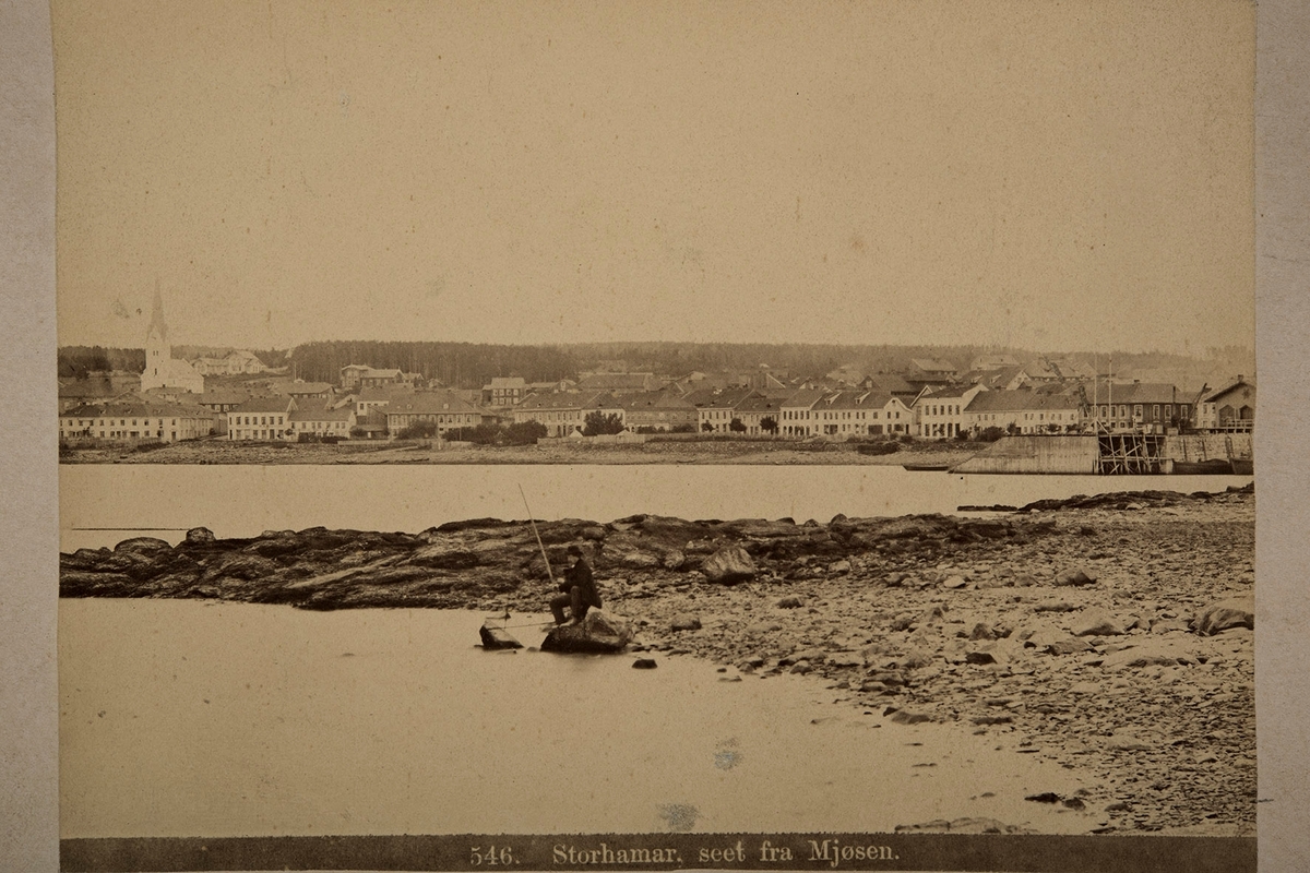 Anno Domkirkeodden, Bypanorama. Fisker på Tjuvholmen. Strandgata med Bekkegata og Simensgården til venstre og Jernbanebrygga til høyre. Hamarbukta. P.A.Thoren Norske Prospekter. 546 "Storhamar seet fra Mjøsen"