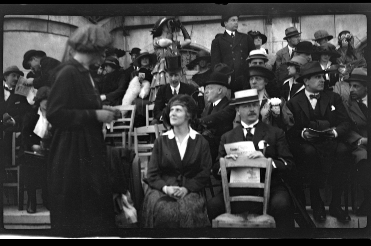 Rolf Sr. Sundt, Hilda Sundt og hennes far Julius Thaulow Aubert, på stoler i første rekke, og mange andre tilskuere på tribune under ukjent arrangement. Fotografert 1919/1920.