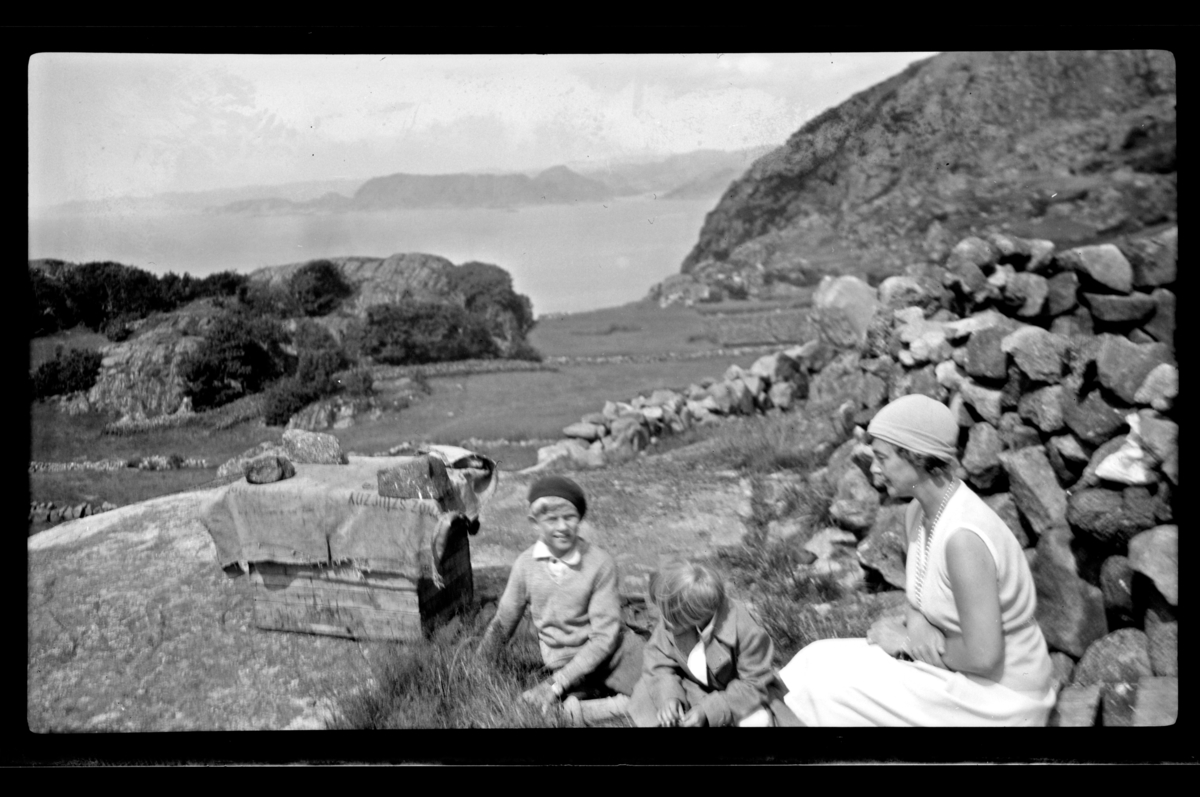 Rolf Sr. Sundt, Rolf Sundt Jr., Eva (?) og Unni Lund Guhnfeldt ved en steinsrøys med utsikt mot sjøen på Vest-Lista. Fotografert juli 1932.