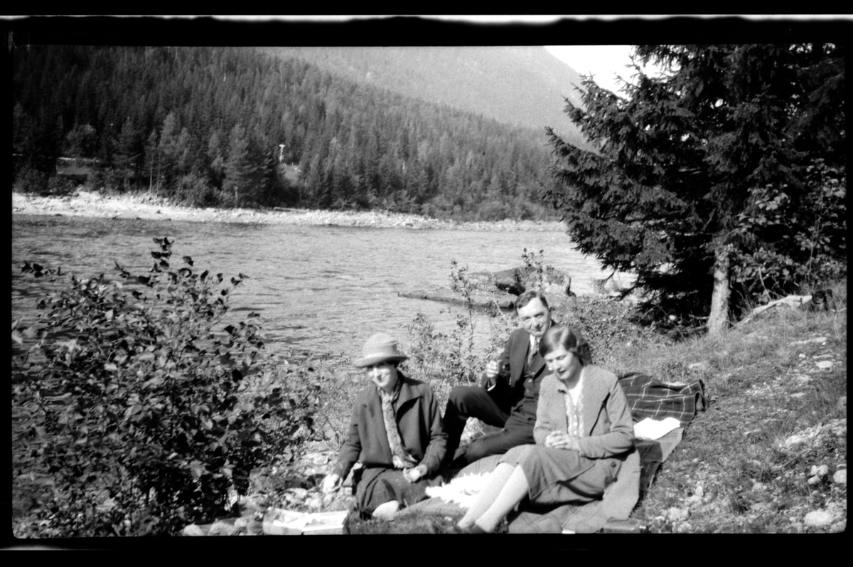 Rolf Sr. Sundt, Ekteparet Agnes og Johan Buratti sitter sammen med Hilda Sundt på et pledd ved en elv. Fotografert 1927.