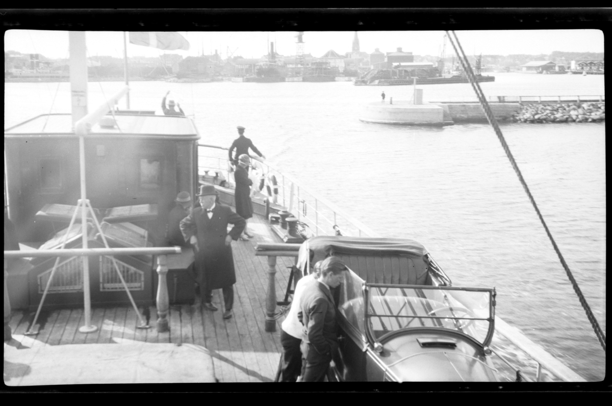 Rolf Sr. Sundt, En bil står på dekket til en båt utenfor en ukjent by. Fotografert 1927.