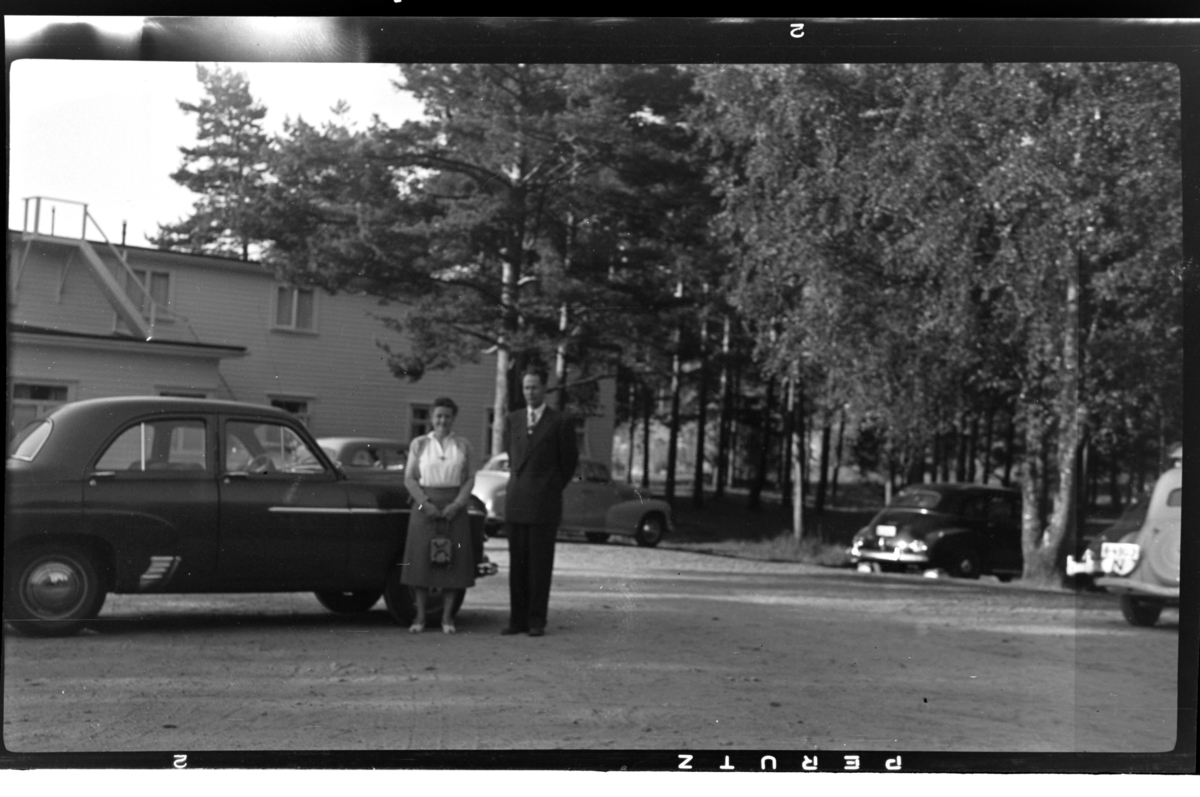 Rolf Sr. Sundt, Et ukjent par står foran en bil. Fotografert ca. 1953.