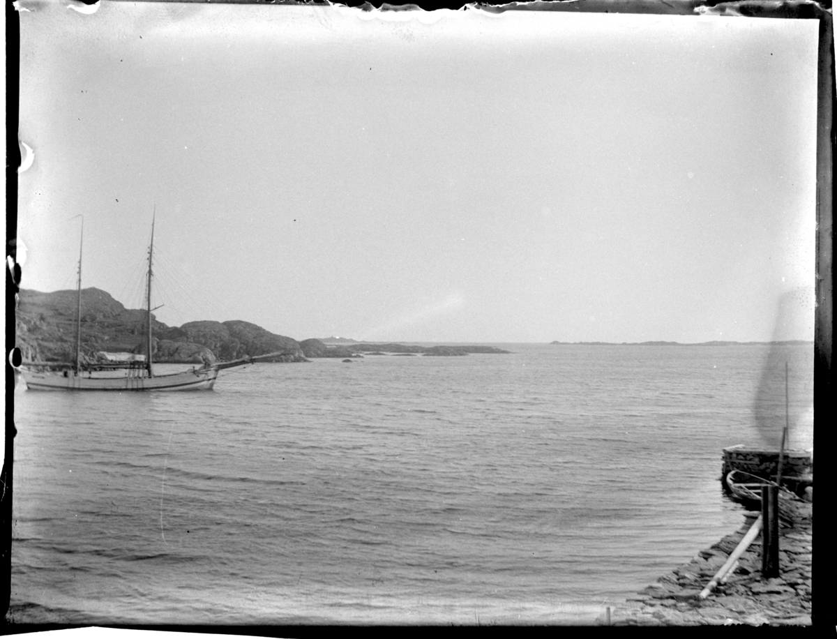 Rolf Sr. Sundt, En seilskute ligger ankret opp innenfor Sandøy, og en robåt ligger ved en brygge i Loshavn; i bakgrunnen sees Einarsneset, Farsund. Fotografert 1900.