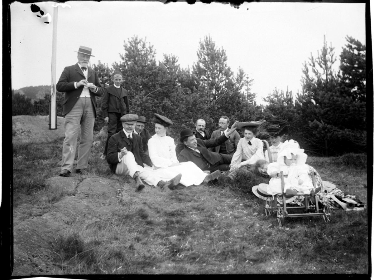 Rolf Sr. Sundt, Konsul Peter Sundt, Peter B. D. Sundt, Trygve Sundt, Rolf Sundt sr., Elisabeth Sundt, ukjent person, Leif Sundt, ukjent person, Mabel Sundt, ukjent person og ukjent person stikker hodet frem på venstre side av barnevognen. Ant. Edna Sundt som sitter i barnevogn, Farø, Farsund Fotografert ca. 1904.