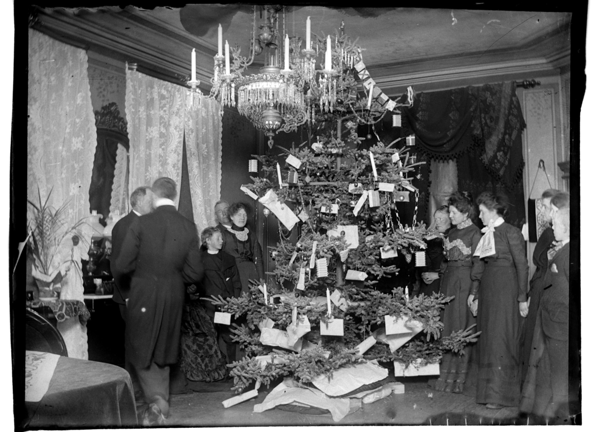 Rolf Sr. Sundt, Mange kvinner, menn og barn står rundt et flott pyntet juletre i en stor stue hos konsul Peter Sundt i Kirkegaten 1, Farsund, Farsund. Fotografert 1900-1903.