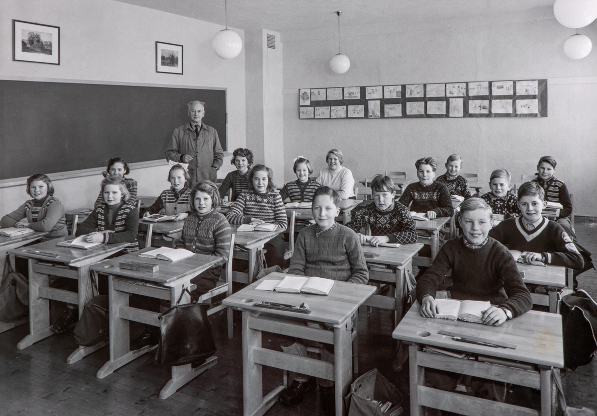 Normann Fotoatelier, Kylstad skole i Furnes. Skoleklasse ved pulter. Undervisning i klasserom. 6. klasse 1954. Kylstad skole sto ferdig til skolestart i 1953. Bildet er av sjette klasse i 1954. I pultrekka til venstre forfra: Marit Skjelseth, Magnhild Skår, bak står skolebestyrer Alf Jensen. Andre pultrekke: Lillemor B…