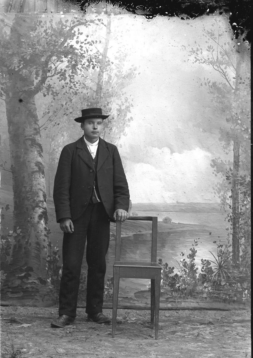 Jakob Jakobsen Engerdal, Ung mann m/hatt, står ved siden av en stol.
