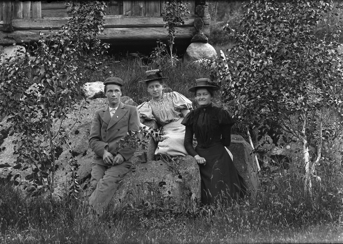 Jakob Jakobsen Engerdal, En mann og to kvinner, sitter ute på en stor stein. Bjørker rundt.