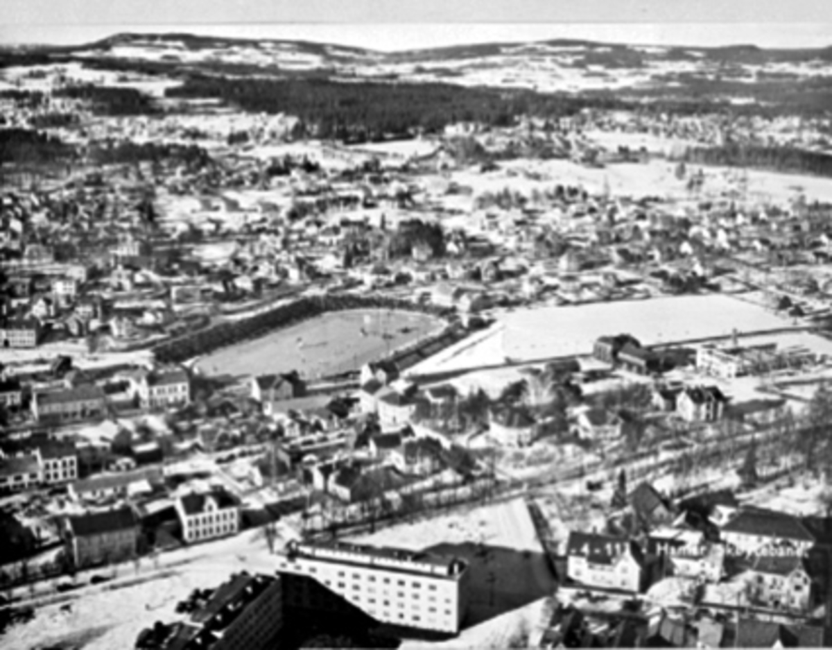 Anno Domkirkeodden, FLYFOTO AV HAMAR SETT MOT NORD, PARKGATA, VANGSVEGEN, ROLSLØKKA, HAMAR STADION FULL AV FOLK, SKØYTELØP, VINTER
