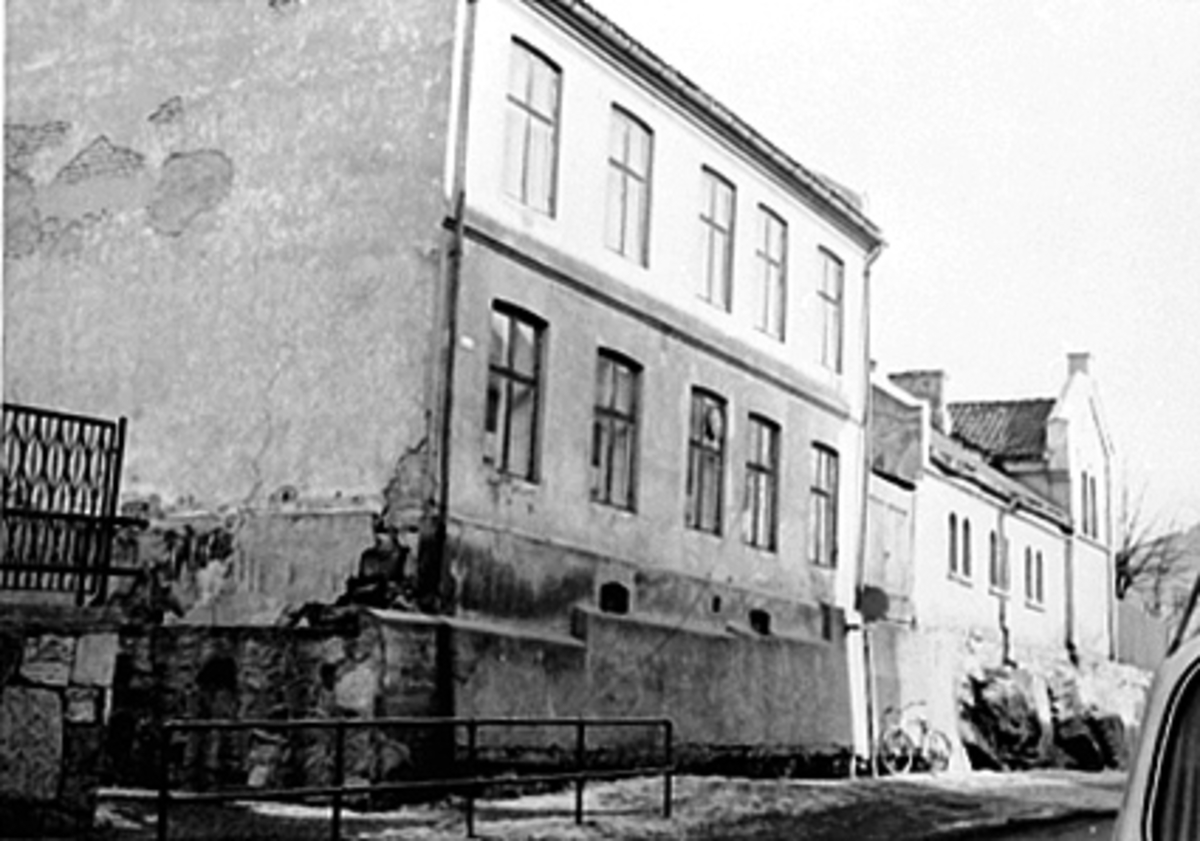 Anno Domkirkeodden, EKSTERIØR MIDTBYEN SKOLE, FOLKESKOLEN MOT SEMINARGATA, SKOLEGATA 1. Inngang til skolegården bak rekkverket mot gaten opp en skråning bak smijernsgjerdet. Vaktmesterbolig og skolekjøkken i det to-etasjers huset midt i bilde.