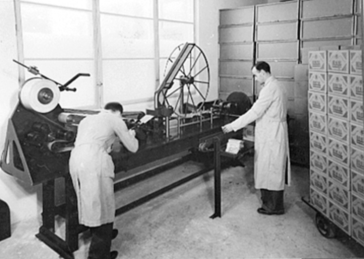 Anno Domkirkeodden, INTERIØR IDEAL FLATBRØDFABRIKK A/S, 2 MENN VED KUVERTPAKKEMASKINEN, KARL OLSTAD TIL HØYRE, VANGSVEGEN 51 I HAMAR.