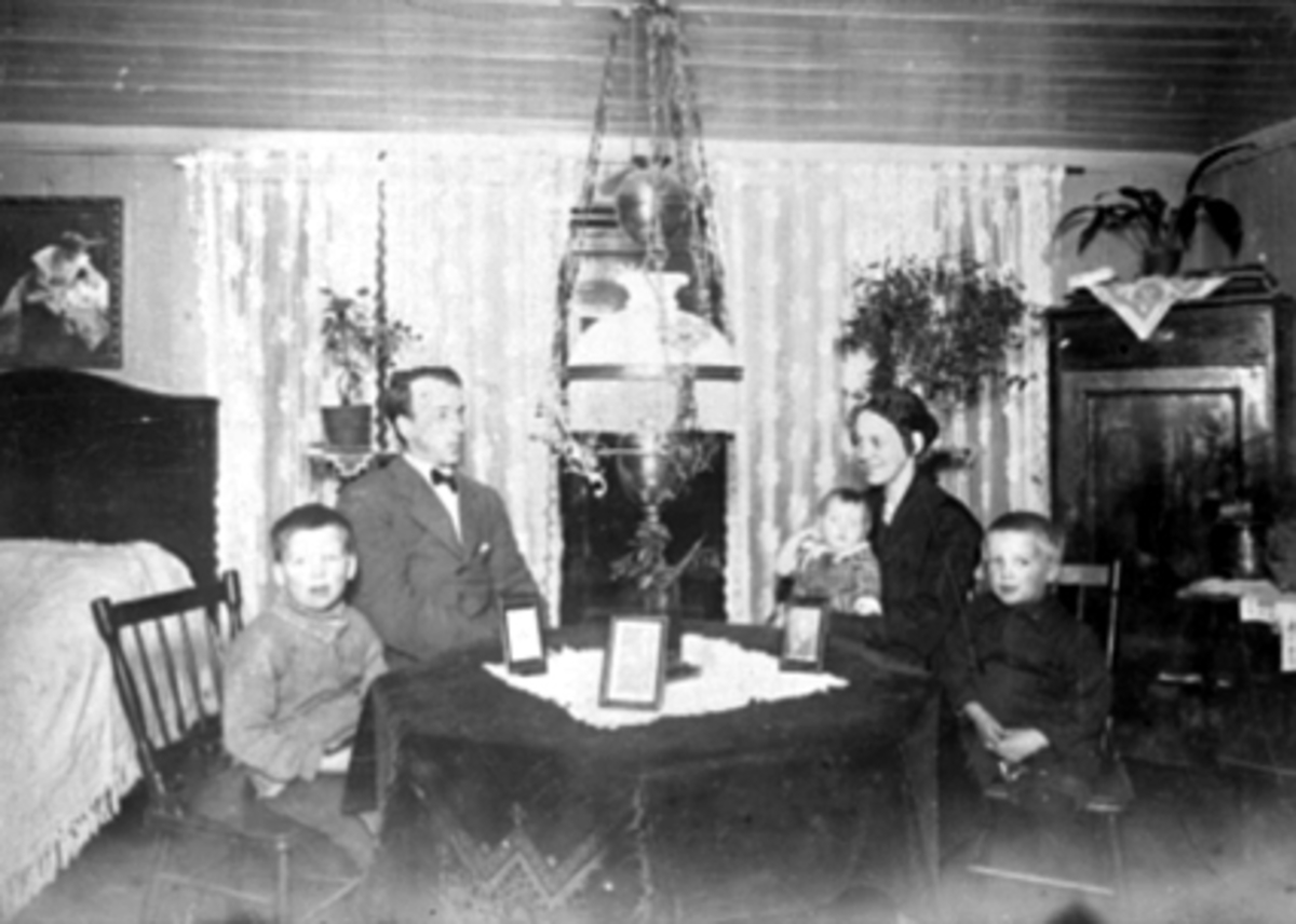 Anno Domkirkeodden, Grønnegata 61, Hamar. Interiør stue, familien Arnesen, seng, hjørneskap, parafinlampe. Fra v: Arvid, Adolf, Gudrun, Ingrid og Gunnar Arnesen. Adolf og Gudrun Arnesen var sterkt engasjert innen Arbeiderpartiet. Var også med på høstrevyene i Hamar Park.