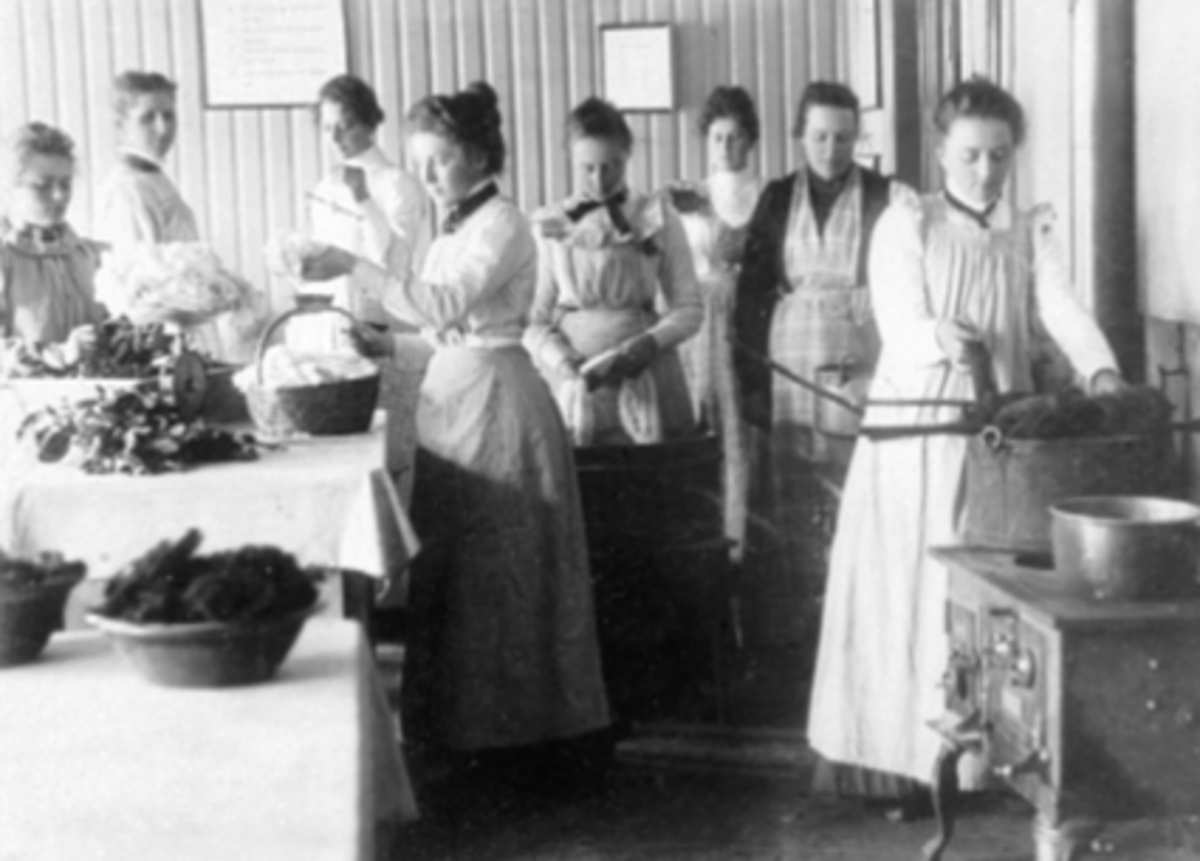 Anno Domkirkeodden, INTERIØR HUSHOLDNINGSSKOLE, GRUPPE 8 UNGE KVINNER I FORKLÆR LAGER MAT, KOKKEKURS, KJØKKEN, NR. 3 FRA HØYRE: ANE HOEL FRA HOL ØSTRE I VANG