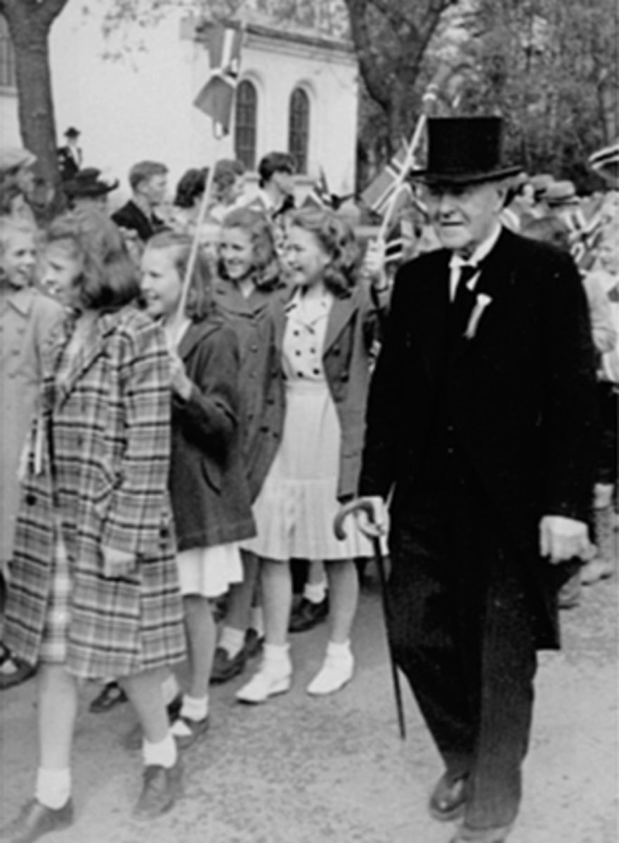 Anno Domkirkeodden, 17. MAITOG, LÆRER ANDREAS NYSETH (KLOKKER I HAMAR), TIL VENSTRE MED ÅPEN KÅPE: ELI KNUTSEN, TIL VENSTRE FOR HENNE: RANDI RØDAHL, FORAN MED FLAGG: ANNELISE RØNNING, MED RUTET KÅPE: JORUN ARNESEN