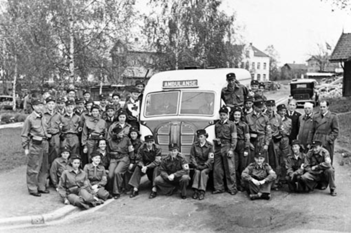 Anno Domkirkeodden, HAMAR RØDE KORS HJELPEKORPS. HJELPEKORPSETS MEDLEMMER SAMLET RUNDT SIN AUSTIN AMBULANSE. Austin, engelsk varebil ombygd til ambulanse, Modellen kom ny i 1946, men reg. nr. D-636 er ikke med i Hvem eier bilen 1948, som kom ut våren det året. Så foto er formodentlig nyere. Hjelpekorpsets første ambul…