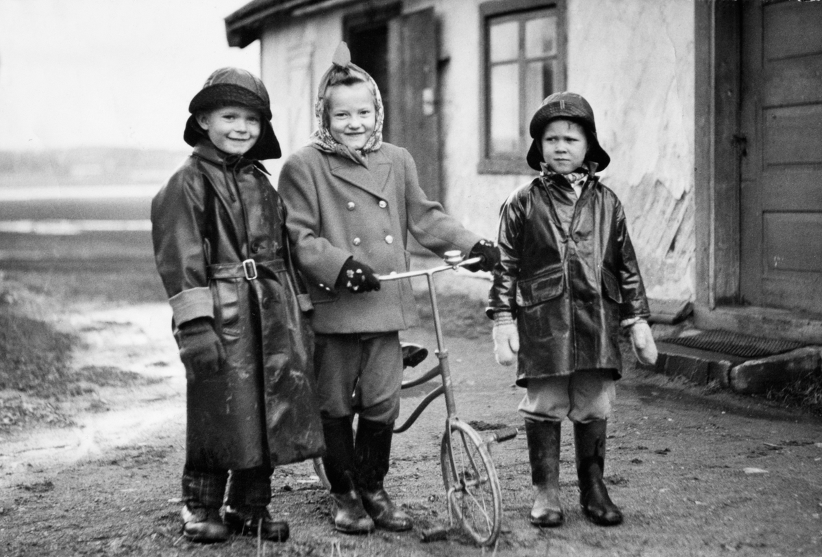 Anno Domkirkeodden, 3 BARN FORAN HUSET TOBRO I BRISKEBYEN, DA VÆRENDE BRISKEBYVEIEN 31, NÅ BRUGATA. FRA V. TROND RUNE DIESEN, ASTRID RUUD, RAGNAR DYRESEN. REGNTØY, SYDVEST. TREHJUL SYKKEL. ASTRID RUUD BODDE I INNGANGEN TIL HØYRE PÅ BILDET. OSKAR KARLSEN BODDE TIL VENSTRE, HAN VAR GÅRDSGUTT PÅ DIESEN GÅRD FREM TIL 1919…