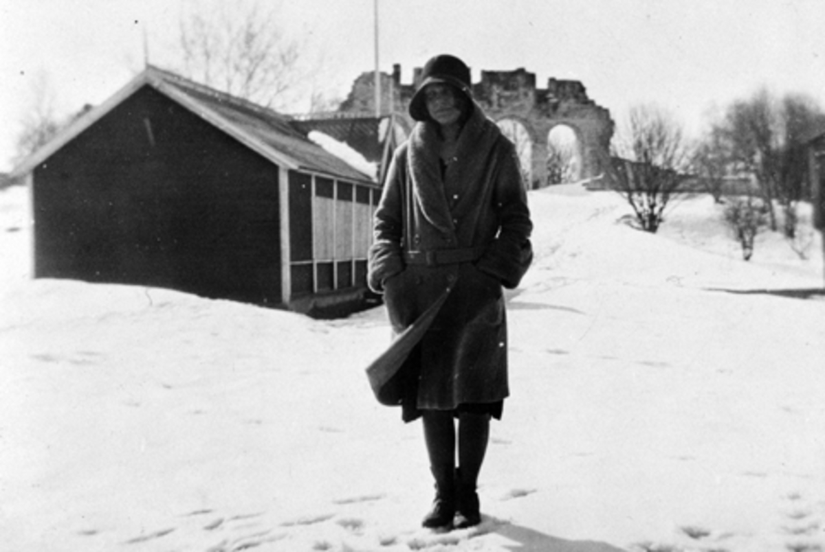 Anno Domkirkeodden, Jenny Olsen (f. Sanden, datter av vaktmester Sanden) er avbildet foran serveringspaviljongen/dansepaviljongen med domkirkeruinen i bakgrunnen. Snødekket landskap. Paviljongen hadde inngang midt på, og inneholdt bord og stoler. På onsdagskvelder var det musikk med bla. Rogneruds trio og Bråthen. Bak…