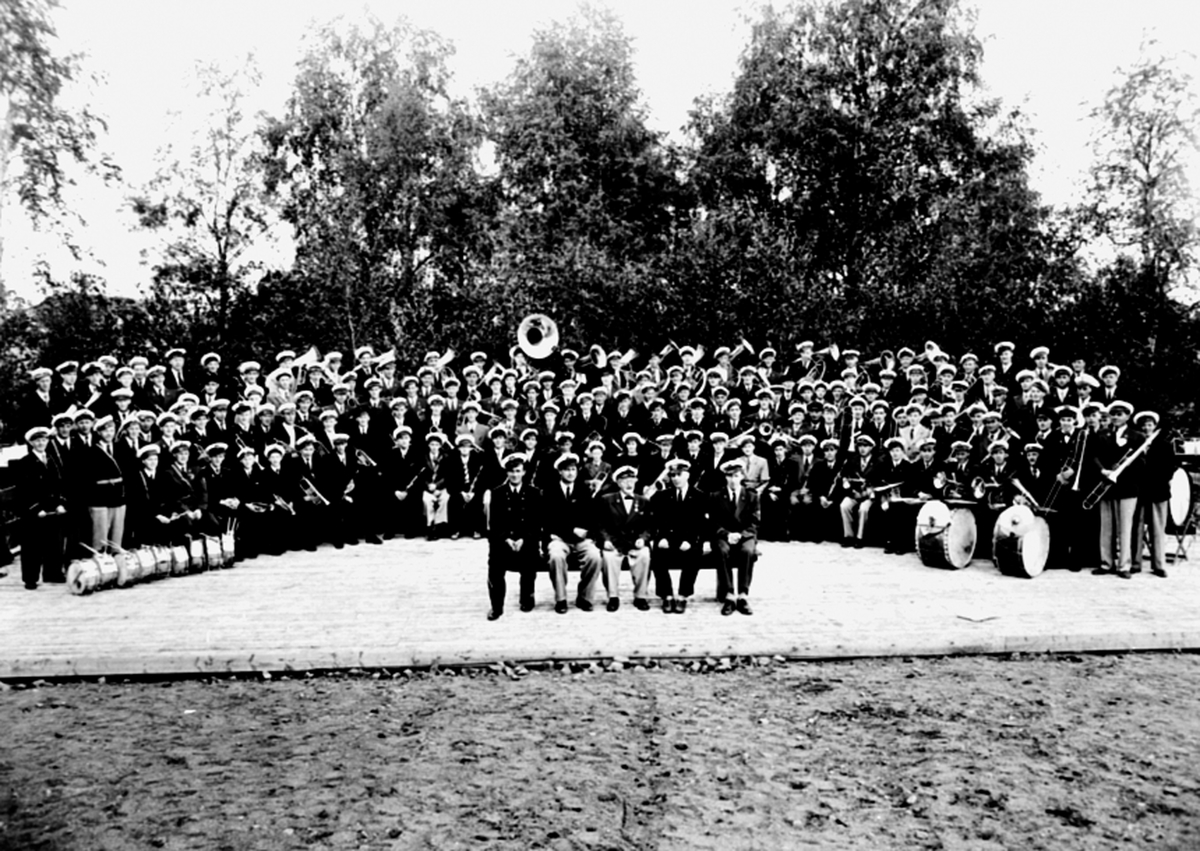 Anno Domkirkeodden, Stor gruppe musikkorps på musikkstevne. Fem dirigenter på benk foran orkesteret. Nes, Hedmark.